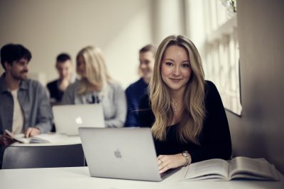 Elev sitter med sin dator och en bok i ett klassrum