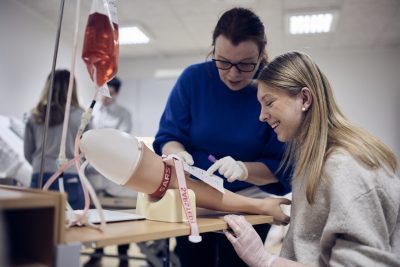 Lärare hjälper elev att ta blodprov på en dockarm