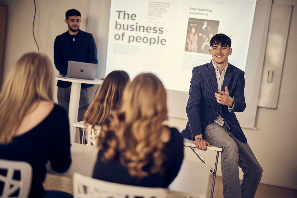 Kille i kavaj sitter på bordskant och håller presentation