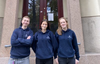 Tre elever i blåa hoodies framför en skolport