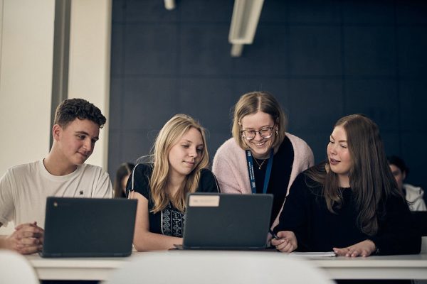 lärare hjälper tre elever med en uppgift