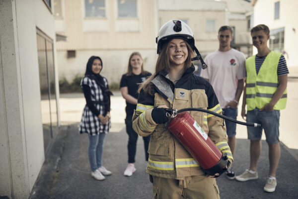 Elev i branduniform håller upp en brandsläckare framför sina vänner