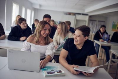 Elever sitter på lektion, en framför en dator och den andra håller i en bok