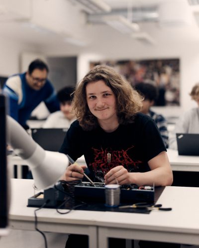 Elev sitter och löder vid en skolbänk