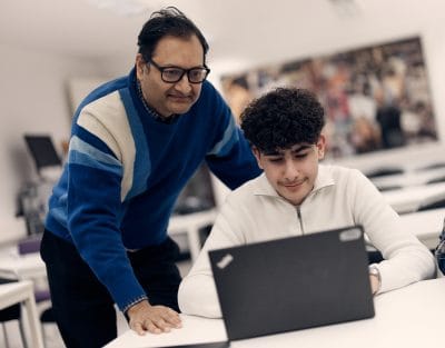 Lärare hjälper en elev som sitter framför sin dator i ett klassrum
