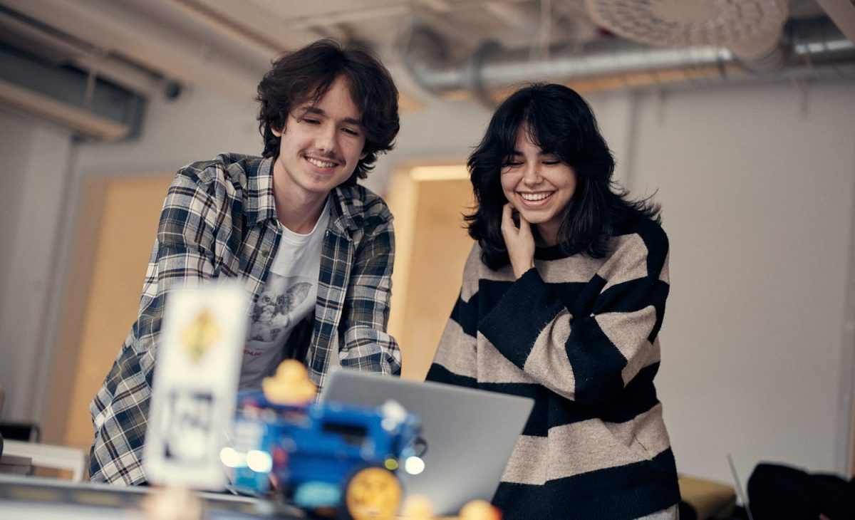 Två elever som ler och kollar på en laptop