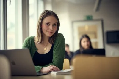 Tjej sitter i ett klassrum och kikar in i kameran