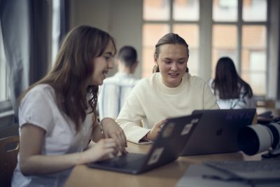 Två elever i ett klassrum med sina datorer